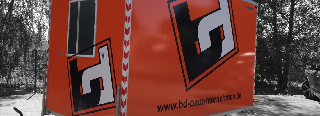 Anhängerbeschriftung BD Bauunternehmen: orangefarbener Bauanhänger mit großem schwarzem Logo und Webadresse – umgesetzt von Folien Fischer Hamburg