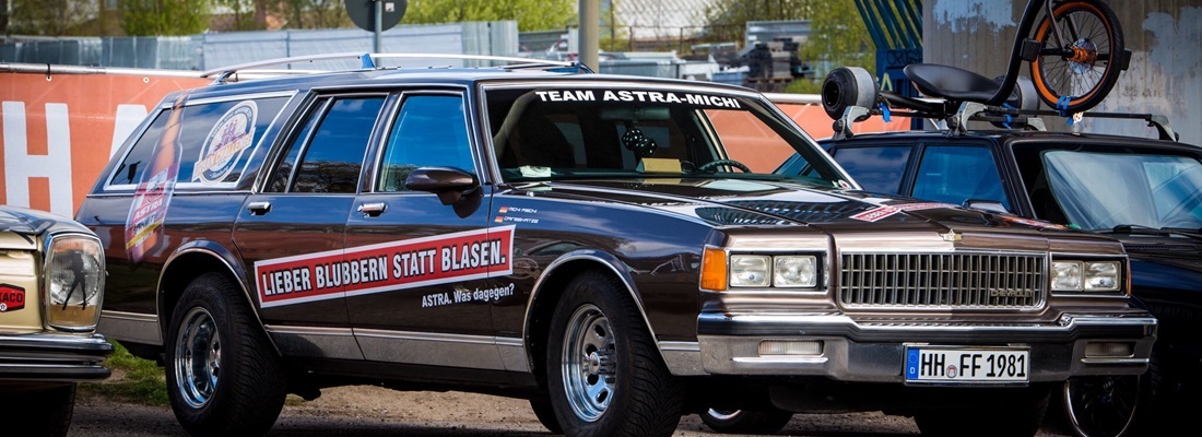 „Fahrzeugbeschriftung Oldtimer-Kombi: schwarzer Wagen mit Slogan ‚Lieber blubbern statt blasen – ASTRA‘, Frontscheibenbanner ‚Team Astra-Michi‘ – umgesetzt von Folien Fischer Hamburg